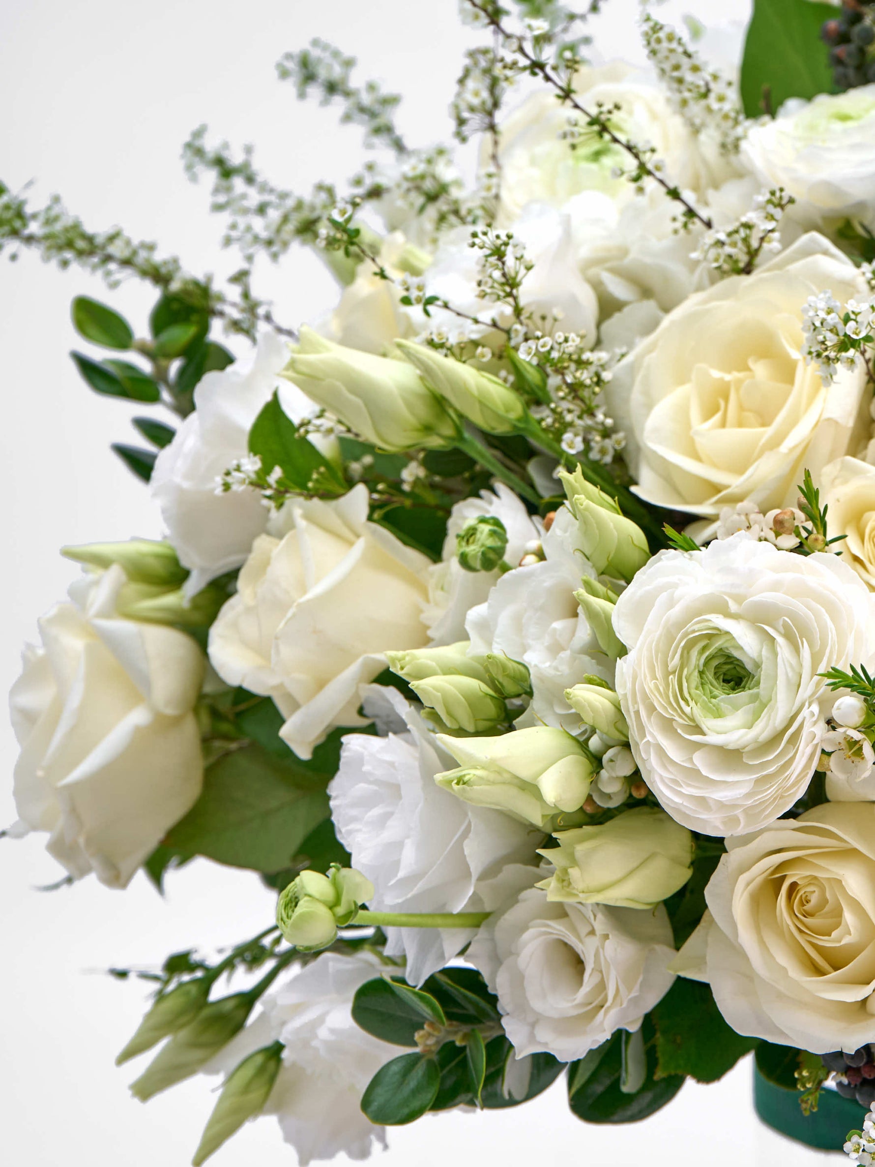 Roses ivoire, renoncules blanches, boutons de lisianthus verts et rameaux fleuris entremêlés