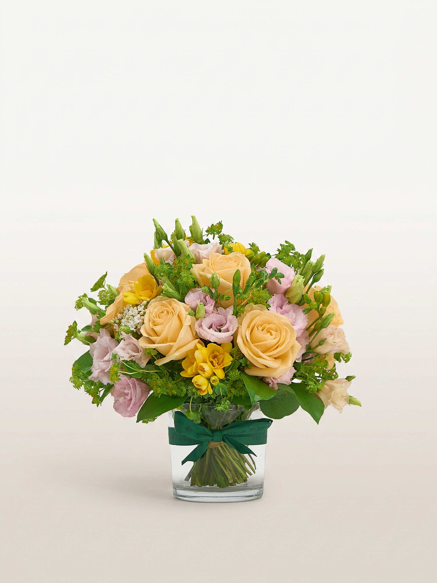 Point du Jour S, roses pêche, lisianthus rose pâle et freesias jaunes dans un vase en verre noué de ruban vert
