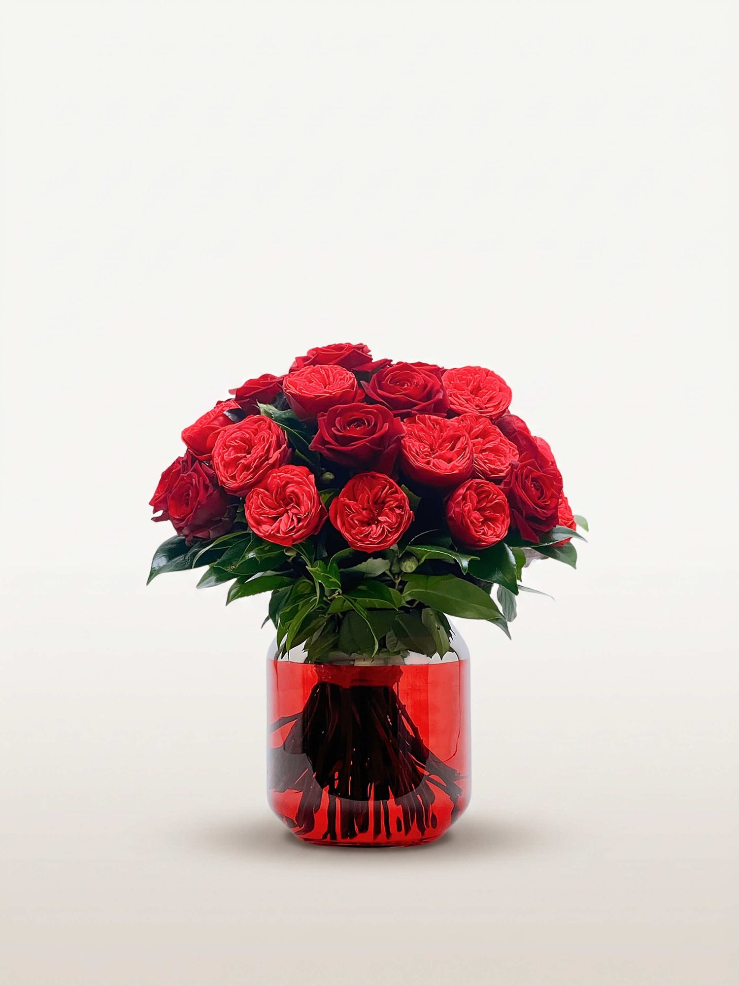 Bouquet rond Cornaline de trente roses rouges et cramoisies, feuillage vert dans un vase rouge translucide