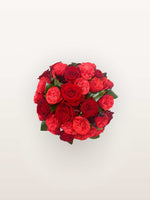 Cornaline, bouquet rond de roses rouges et roses rubis en boutons denses, feuillage vert entre les fleurs