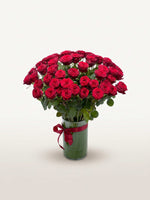 Royal N°50 réunit une brassée généreuse de roses rouges veloutées dans un vase en verre noué d'un ruban rouge