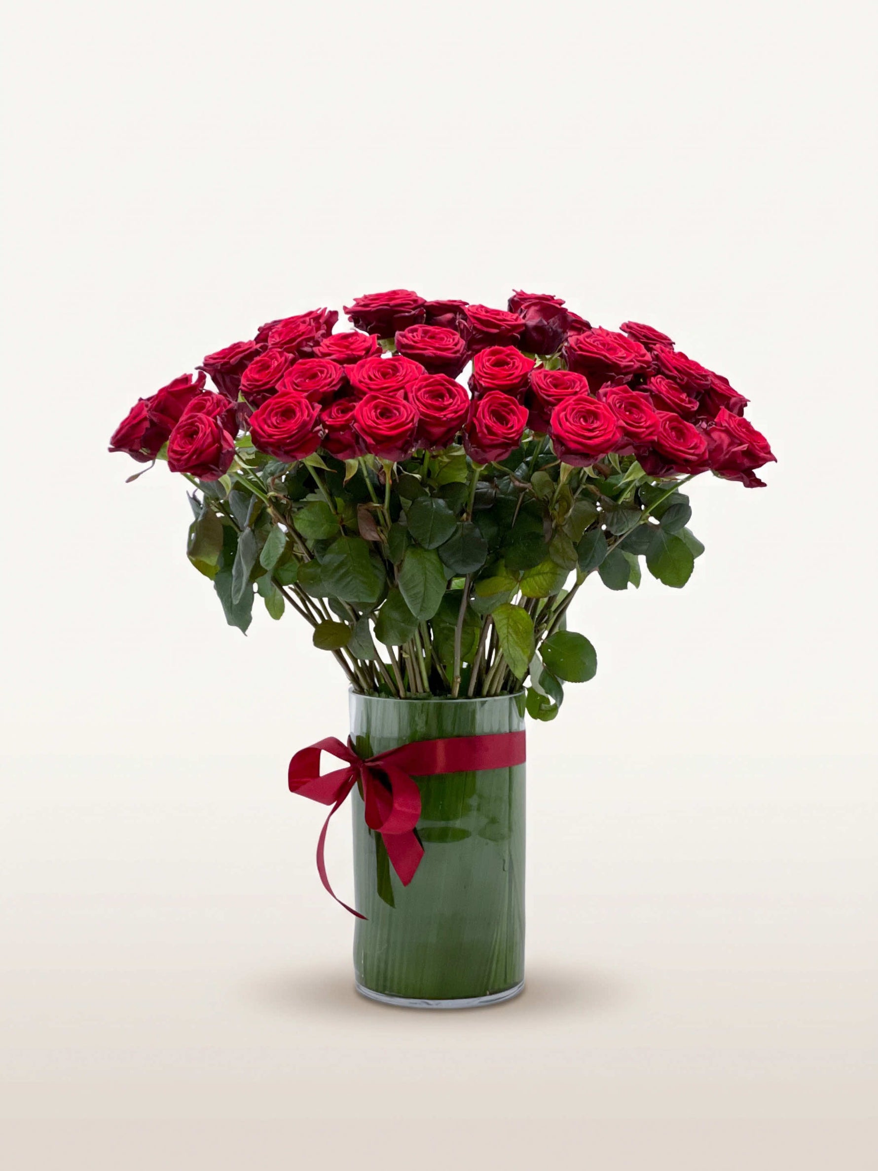 Royal N°75 dévoile une brassée XL de roses rouge velouté dans un vase cylindrique noué d'un ruban carmin