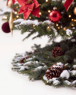 Pied du sapin de Noël Grand Apparat Opéra : branches de sapin posées au sol, pommes de pin et neige artificielle 