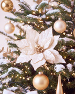 Détail du sapin de Noël Grand Apparat Sacré-Cœur : poinsettia ivoire et boules dorées sur branches enneigées 